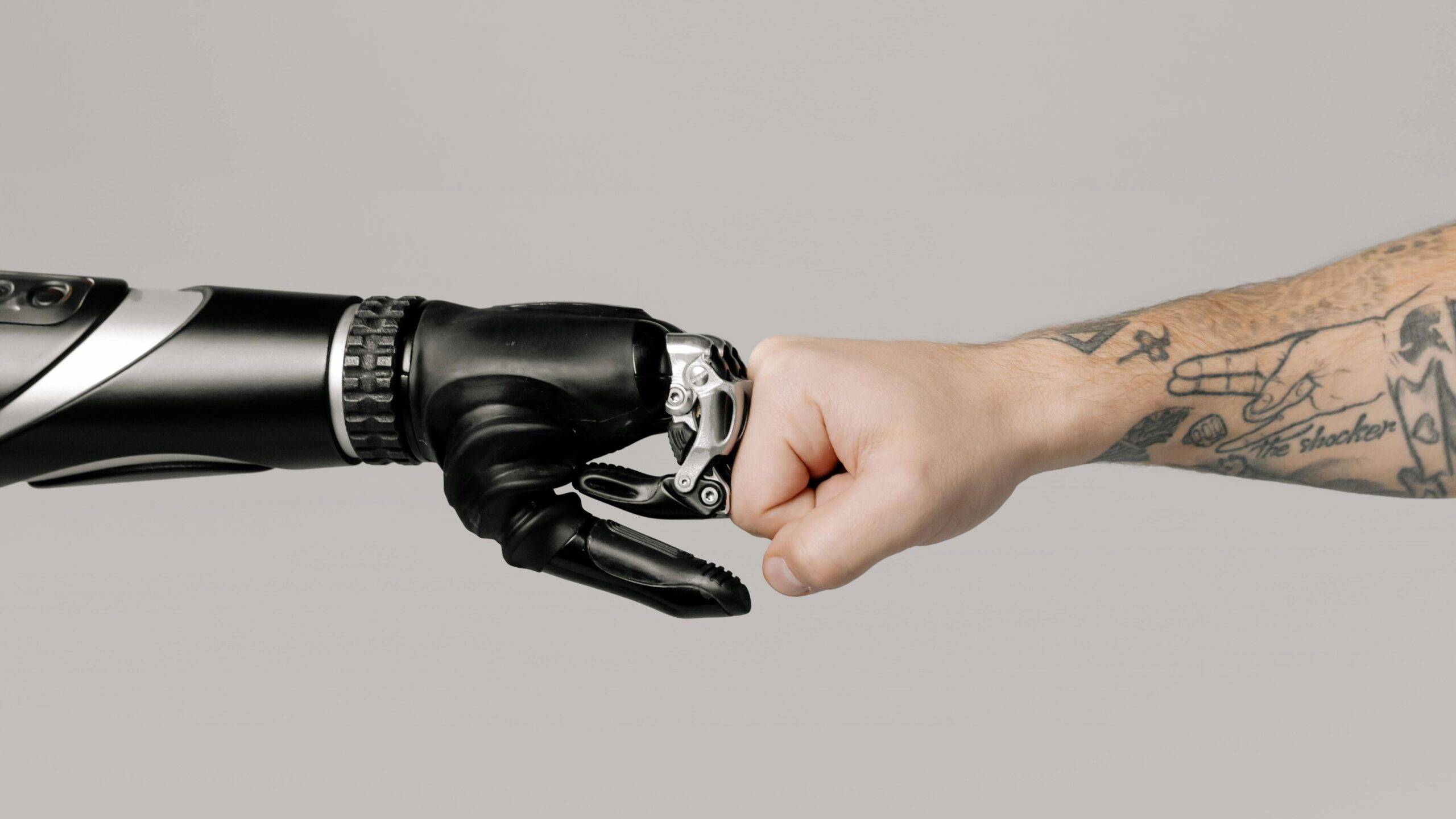 A human fist bumping with a prosthetic arm on a neutral background.